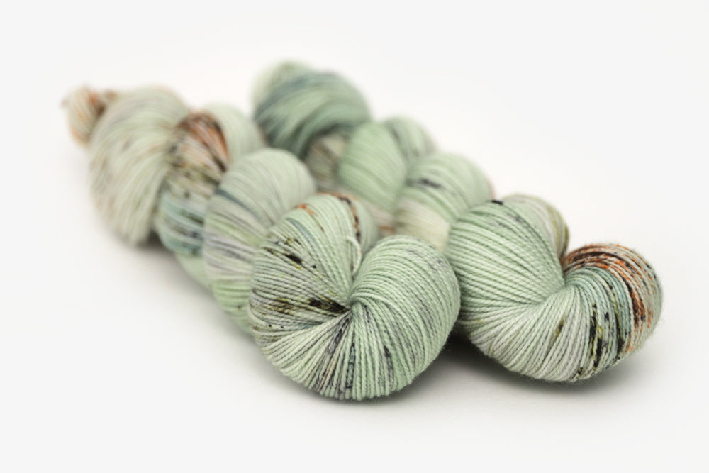 speckled hand dyed pale green sage peach merino sock yarn